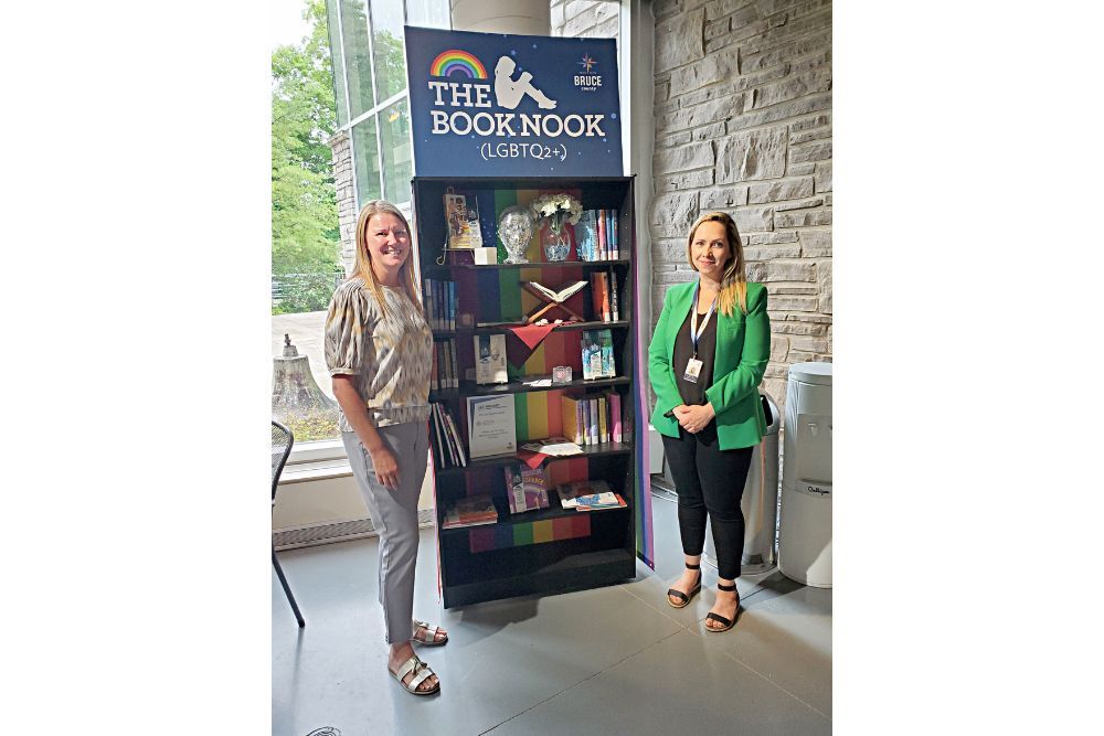 Jen Isber-Legge, Grants and Donor Relations Coordinator for Community Foundation Grey Bruce, and Renata Bell, Development Officer with the Bruce County Museum and Cultural Centre, stand in front of the LGBTQ2+ Book Nook.